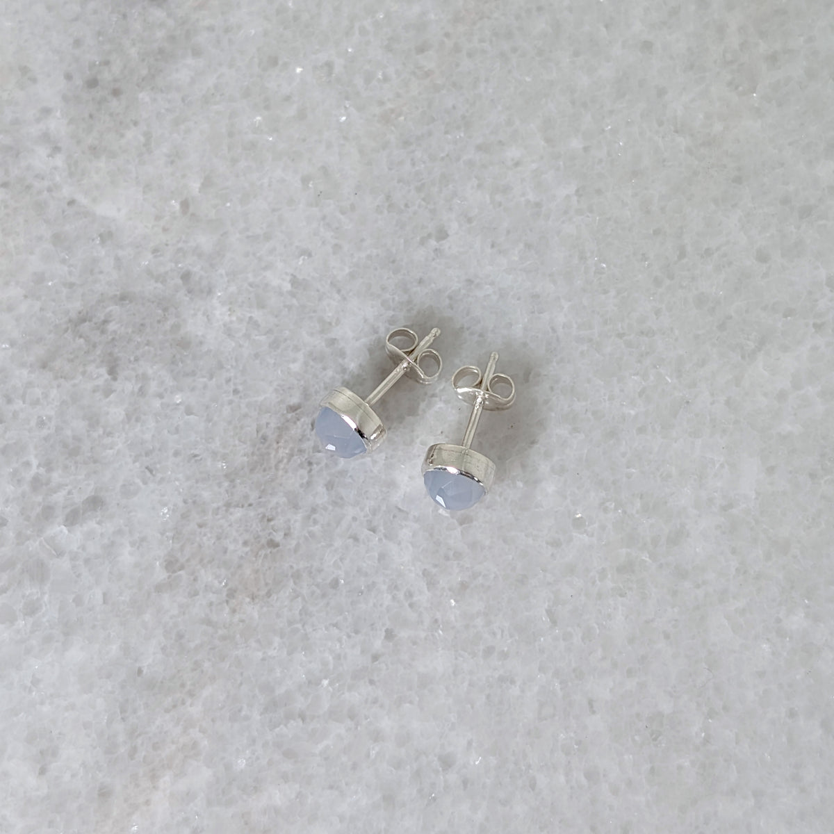 Side view of a pair of round chalcedony rose cut cabochons set in silver studs on a marble surface
