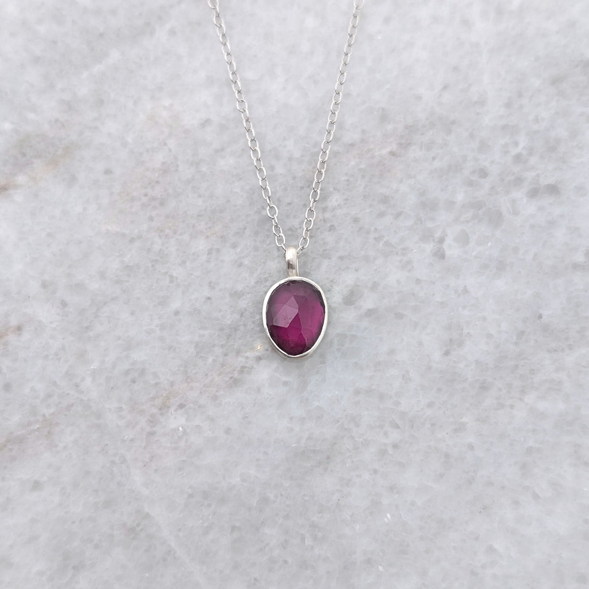 Silver necklace with a warm purple stone pendant on a white marble surface