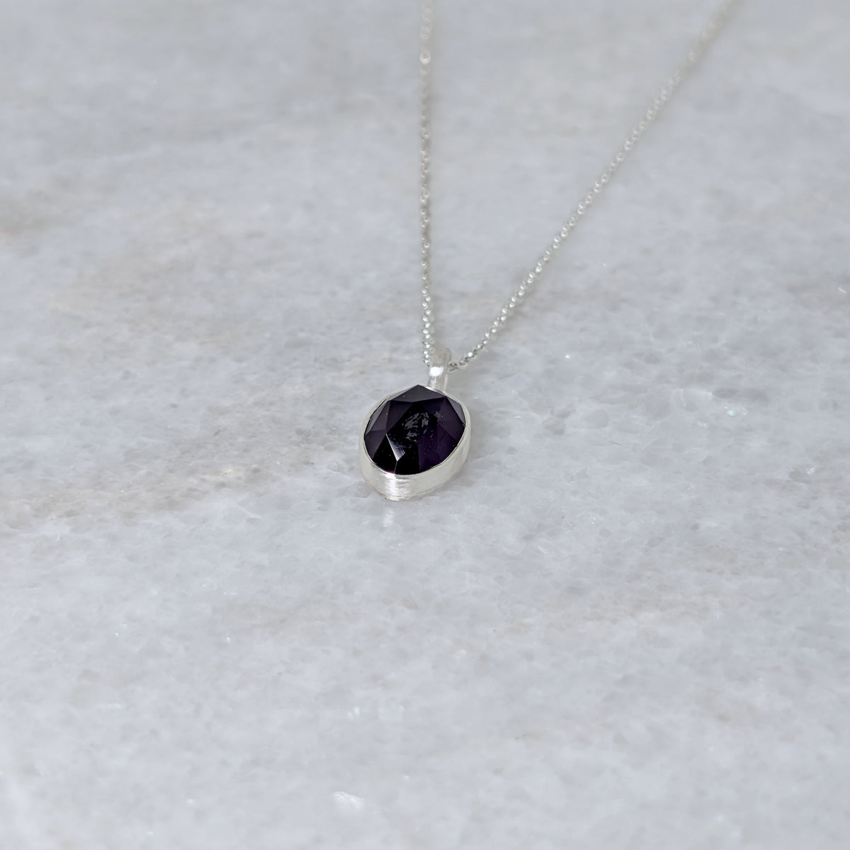 Angled view of Silver necklace with a purple stone pendant on a marble surface