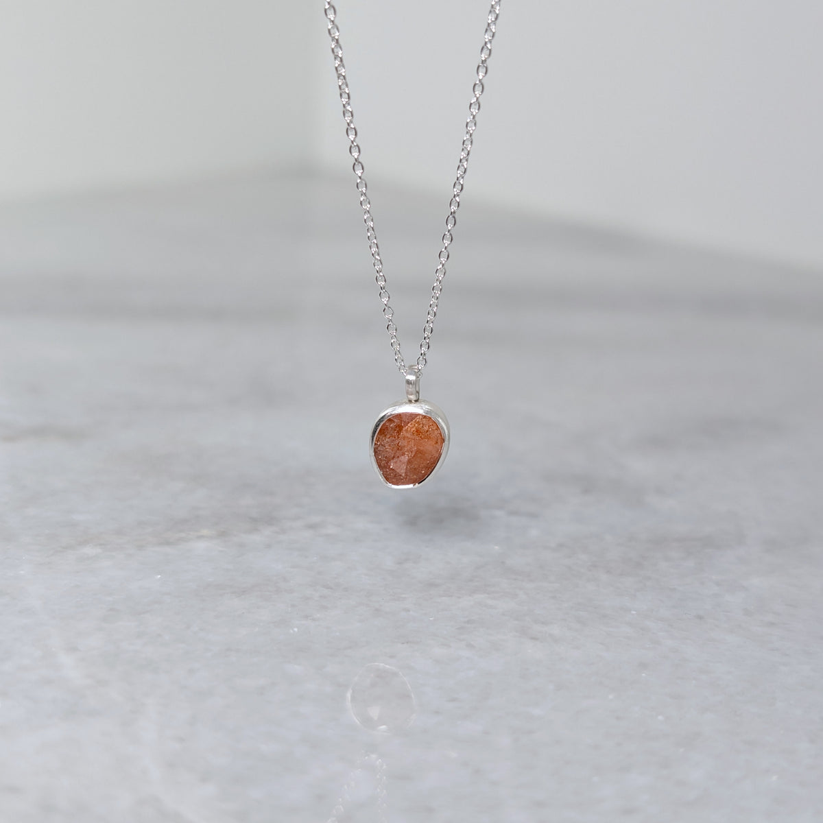 Silver necklace with an orange stone pendant on a white marble background