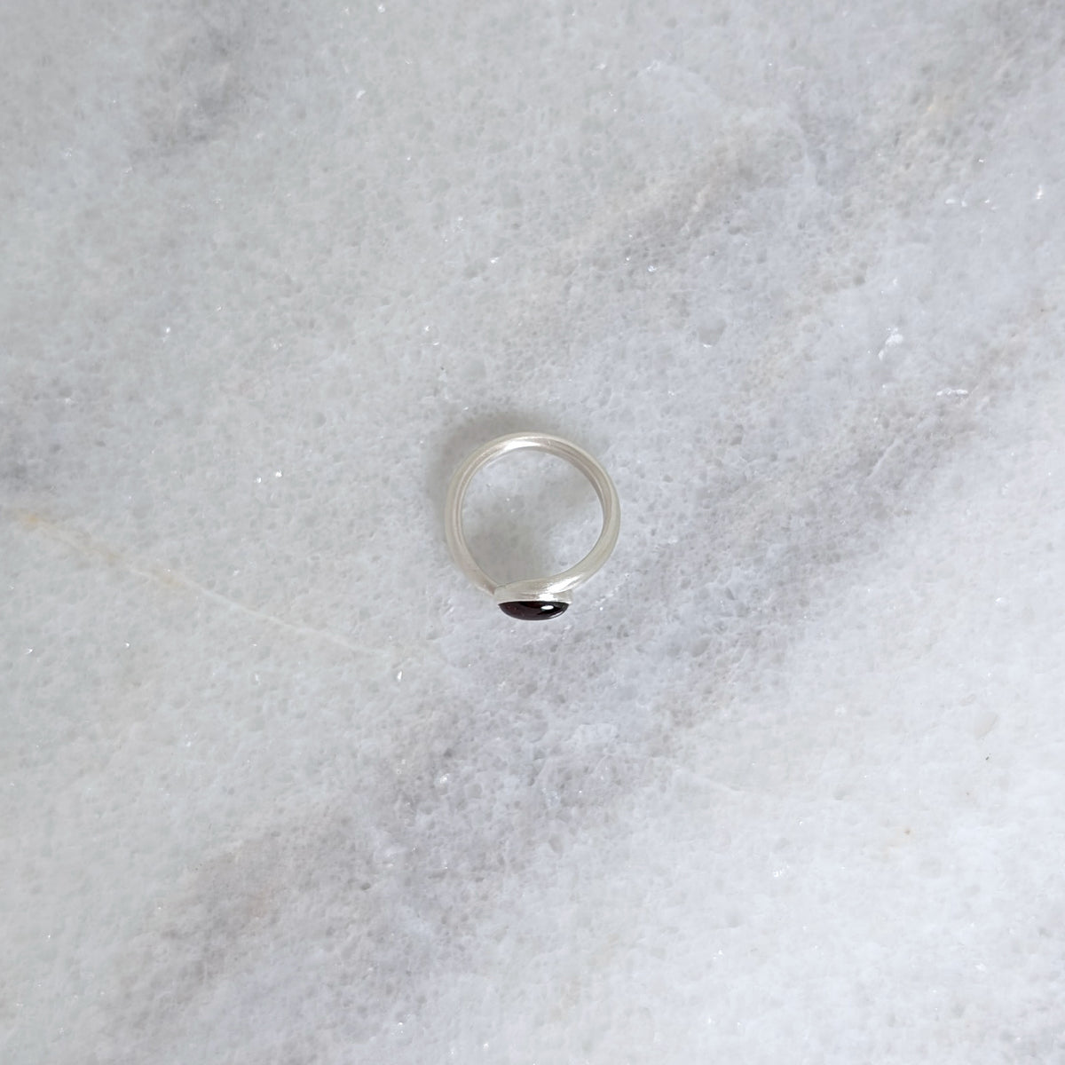 Side view of silver ring with bezel set red garnet cabochon on a grey marble background