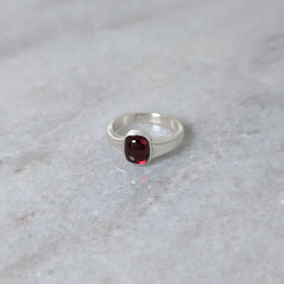 Angled view of silver ring with a garnet center stone on a white marble surface