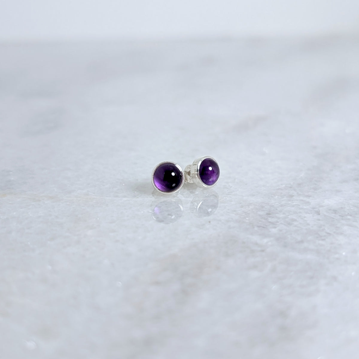 Amethyst stud earrings on a white marble surface