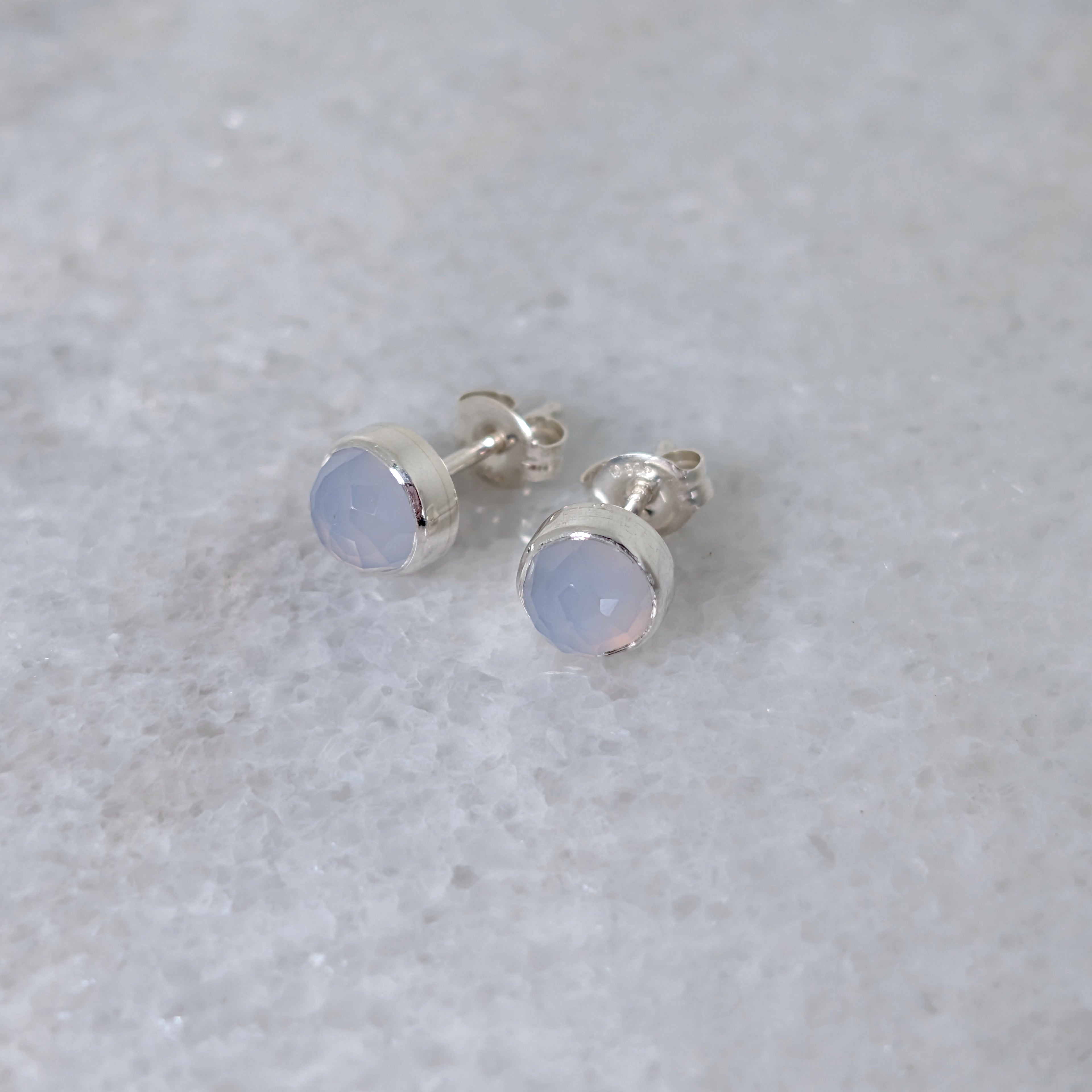 A pair of round chalcedony rose cut cabochons set in silver studs on a marble surface