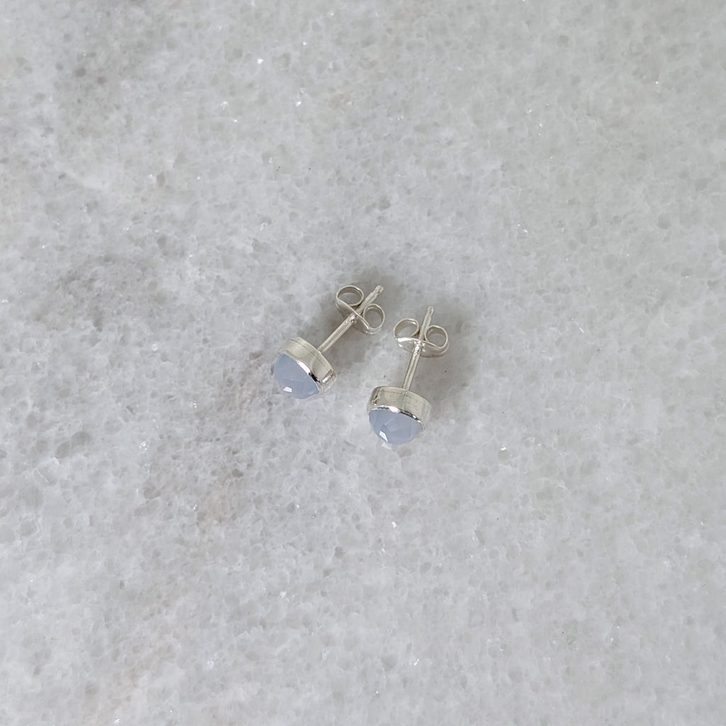 Side view of a pair of round chalcedony rose cut cabochons set in silver studs on a marble surface