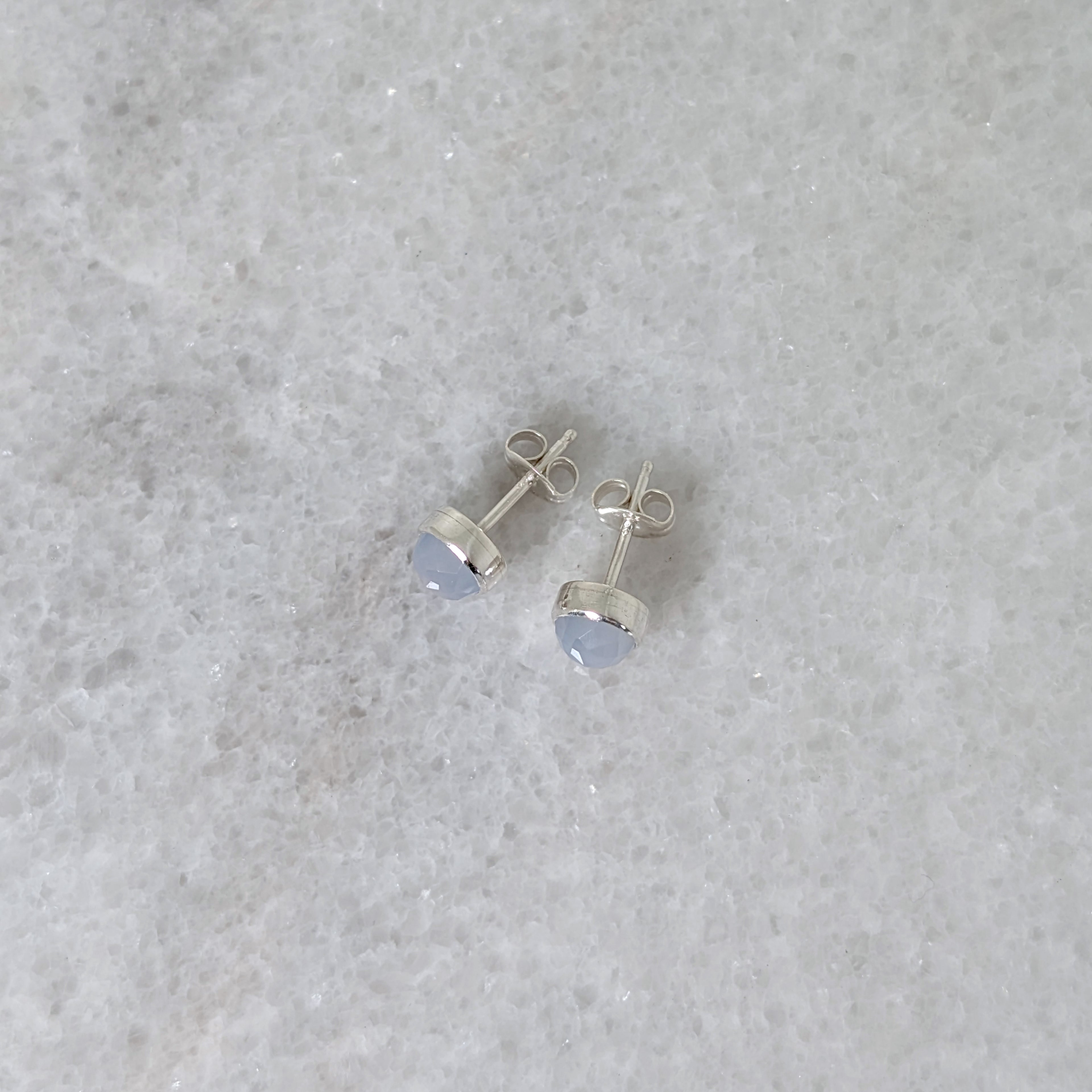 Side view of a pair of round chalcedony rose cut cabochons set in silver studs on a marble surface