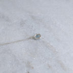 Back view of silver bezel with a windowed view of the light blue speckled stone with two vines framing it on a white marble sruface