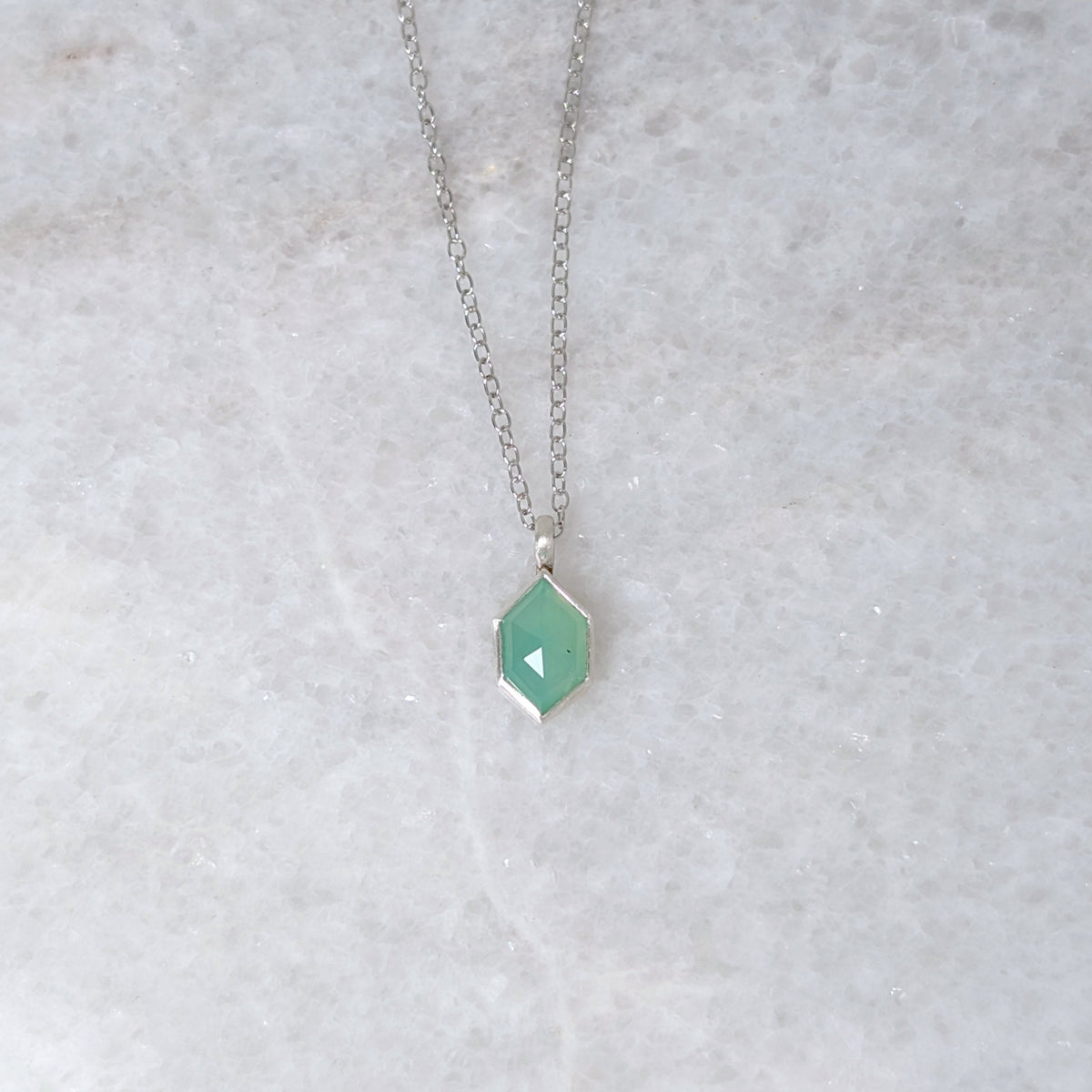 Necklace with a green hexagonal pendant on a white marble background