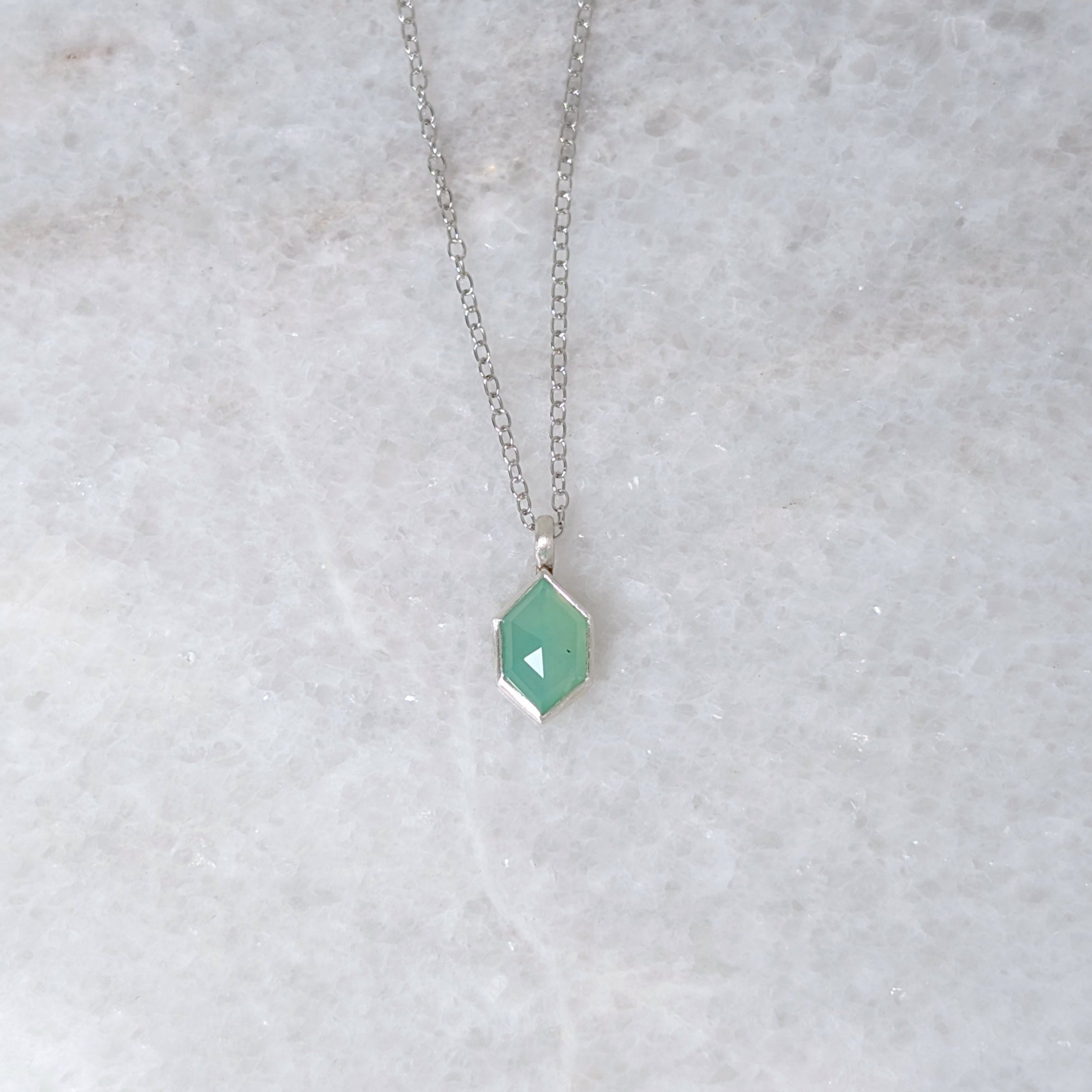 Necklace with a green hexagonal pendant on a white marble background