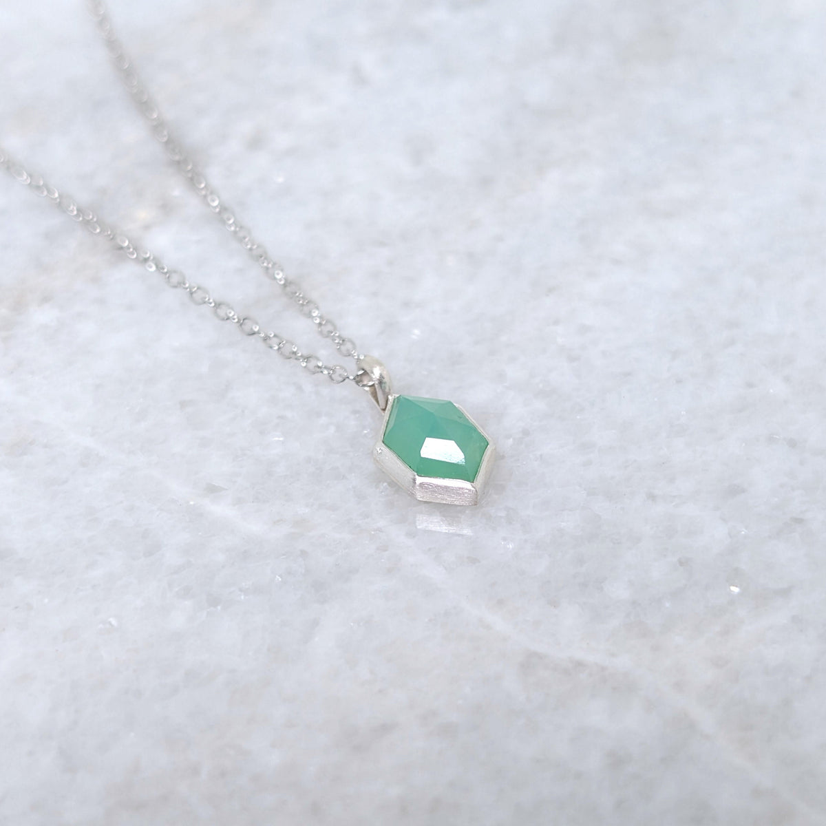 Necklace with a green hexagonal pendant on a white marble background