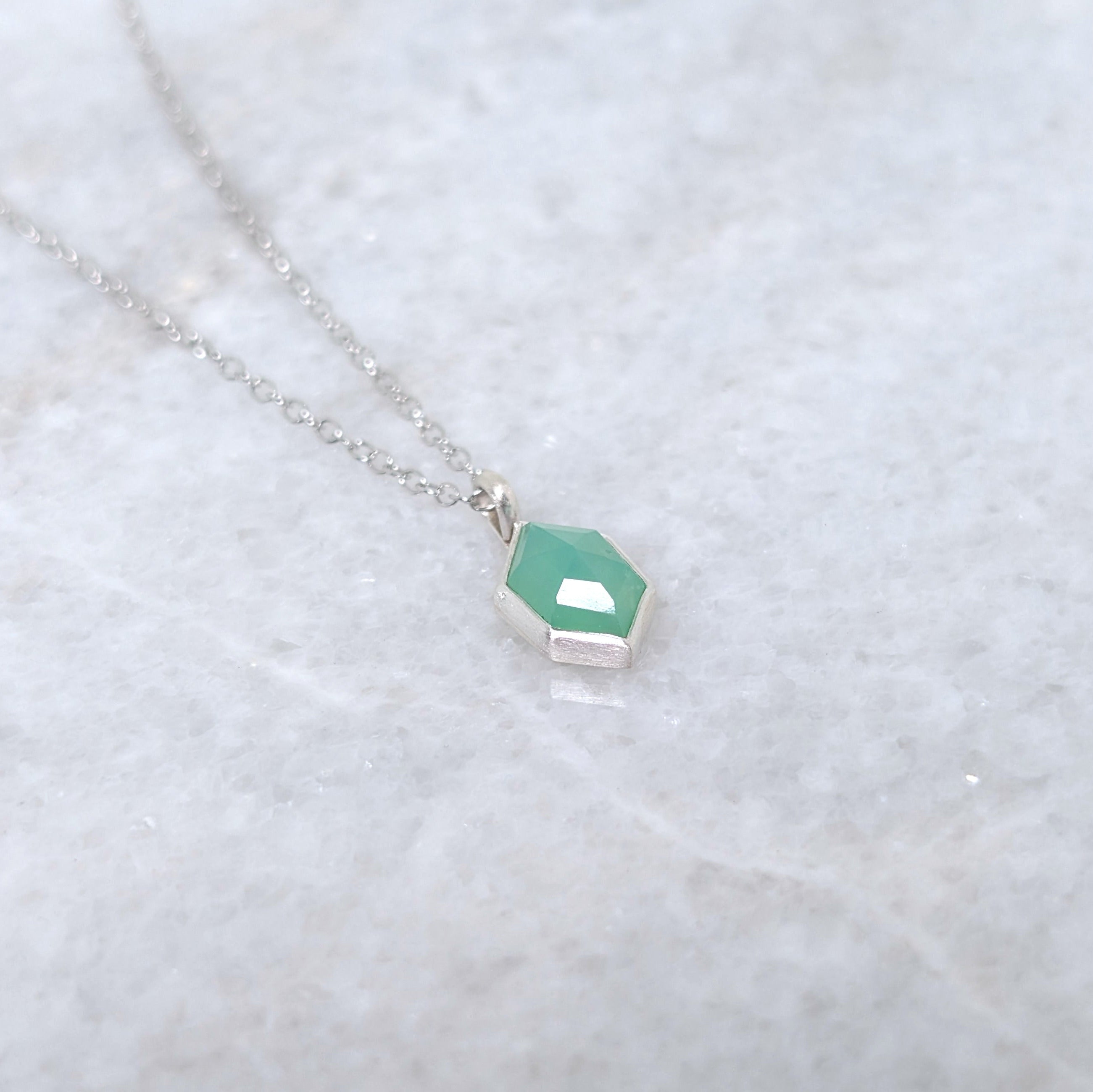 Necklace with a green hexagonal pendant on a white marble background