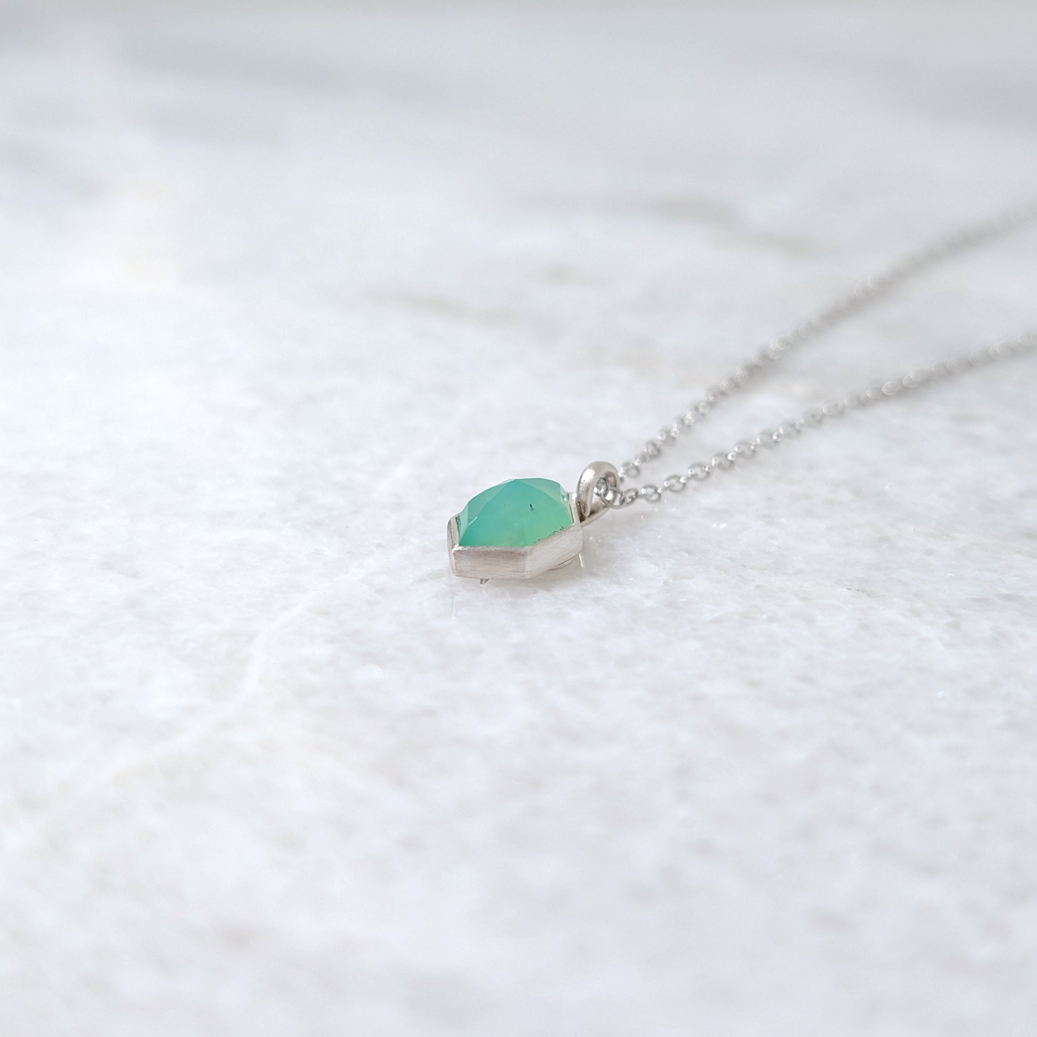Necklace with a green hexagonal pendant on a white marble background