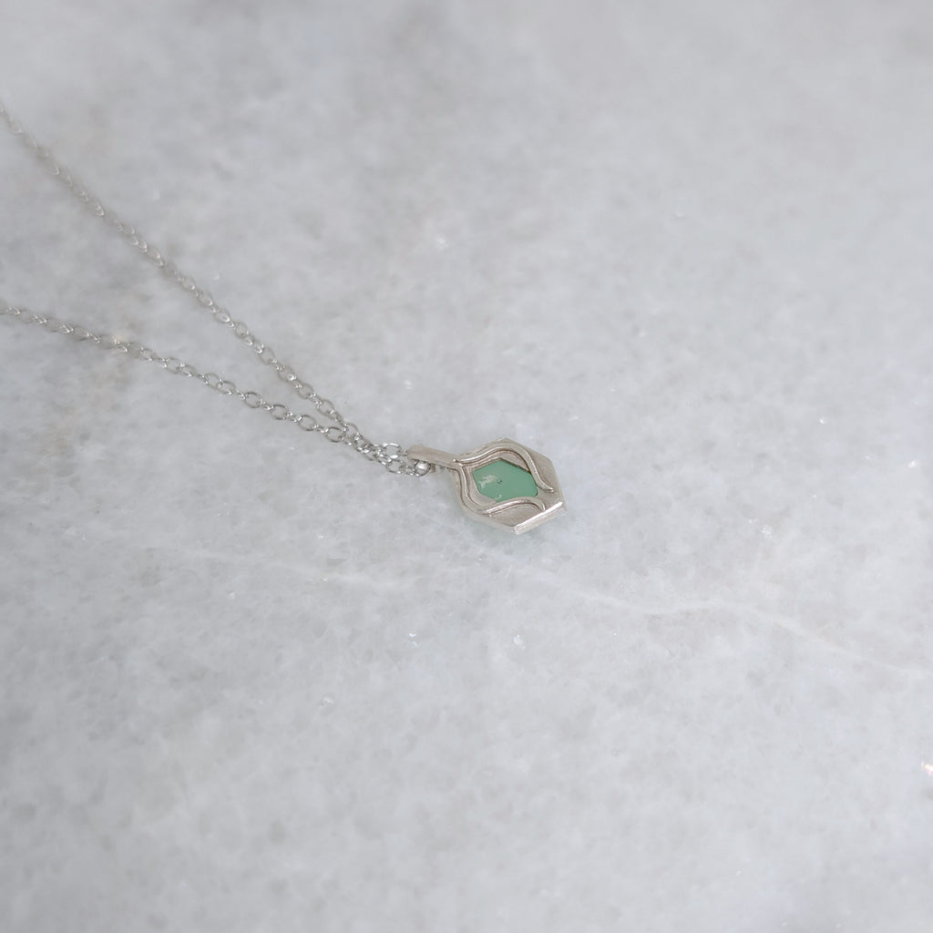 Back view of green pendant with a window framed by two vines on a white marble background