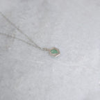 Back view of green pendant with a window framed by two vines on a white marble background