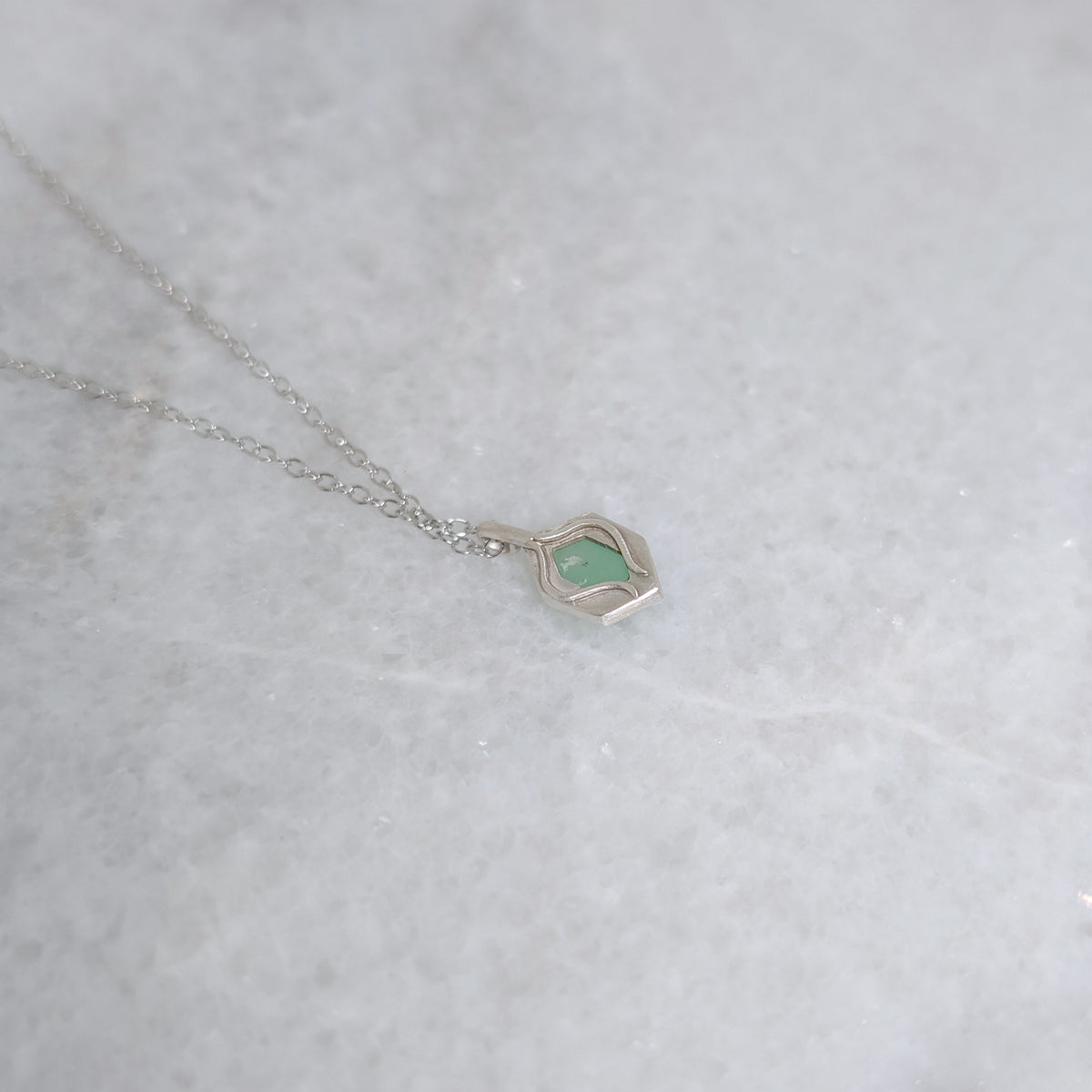 Back view of green pendant with a window framed by two vines on a white marble background
