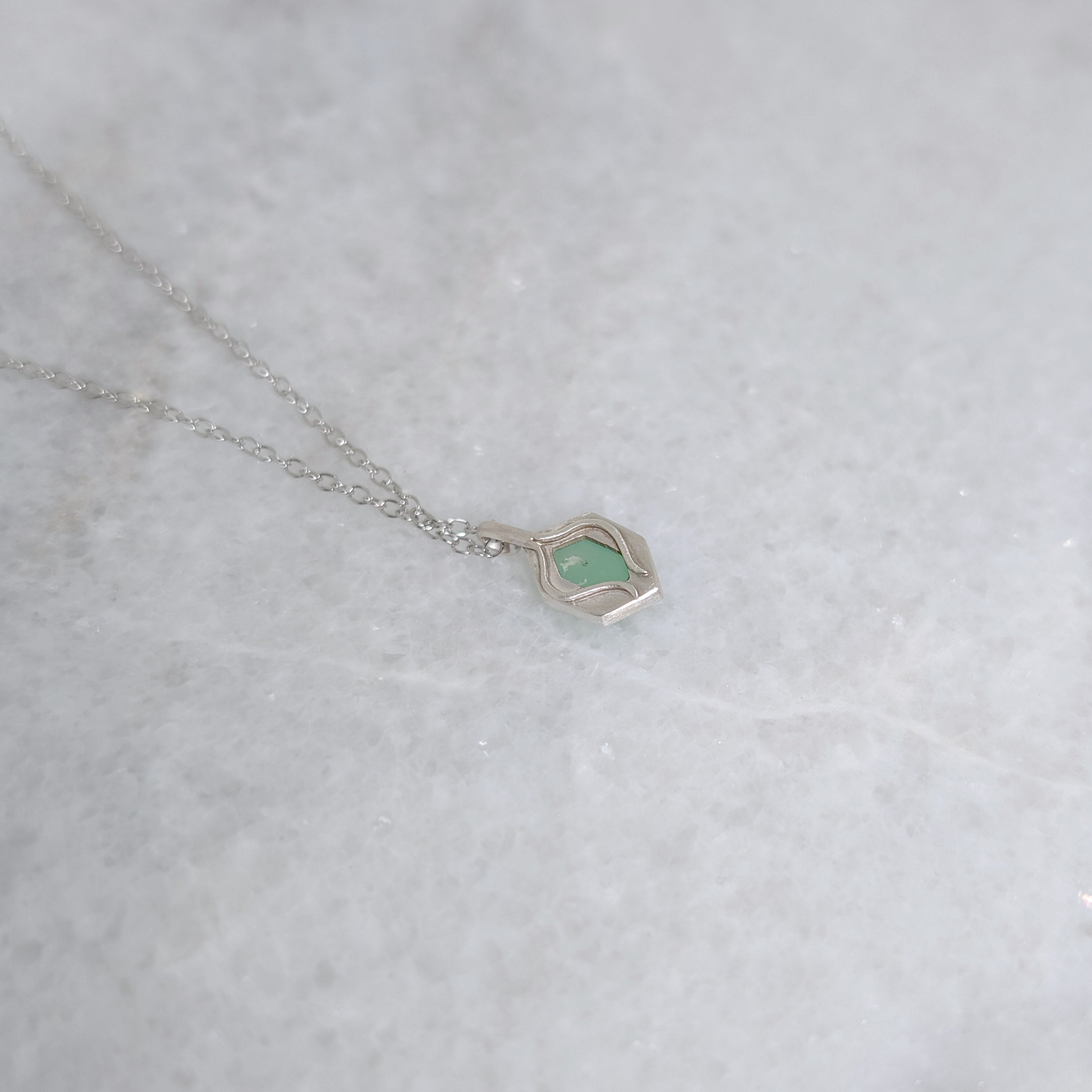 Back view of green pendant with a window framed by two vines on a white marble background