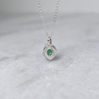 Back view of a grass green stone pendant in a silver windowed bezel with silver vines curling over it, hanging over a white marble surface