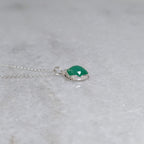 Side view of a grass green stone pendant in a silver scalloped edge bezel with curls of silver vines around the sides, on a white marble surface