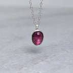 Silver necklace with a warm purple stone pendant hanging over a white marble surface
