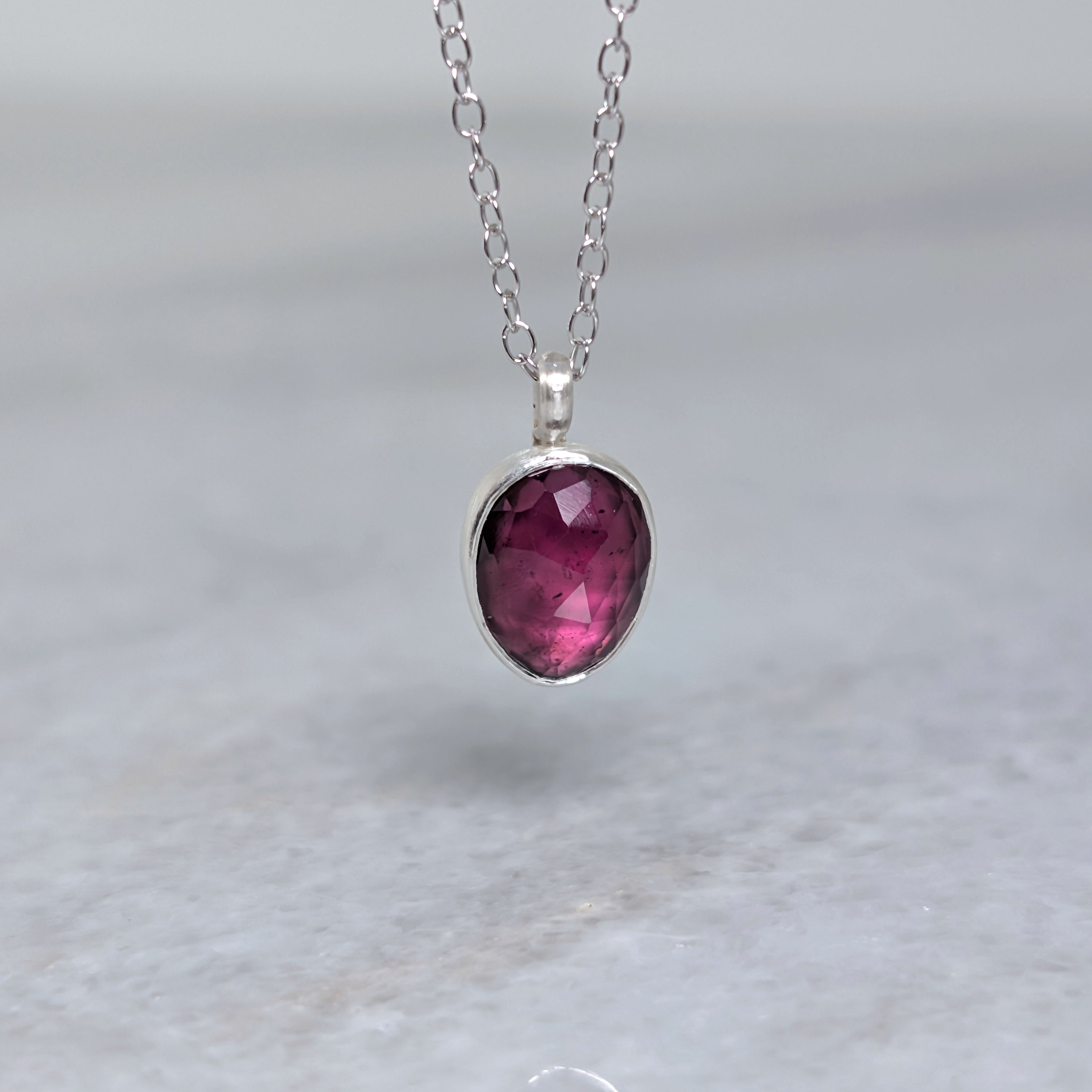 Silver necklace with a warm purple stone pendant hanging over a white marble surface