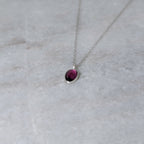 Silver necklace with a warm purple stone pendant on a white marble surface