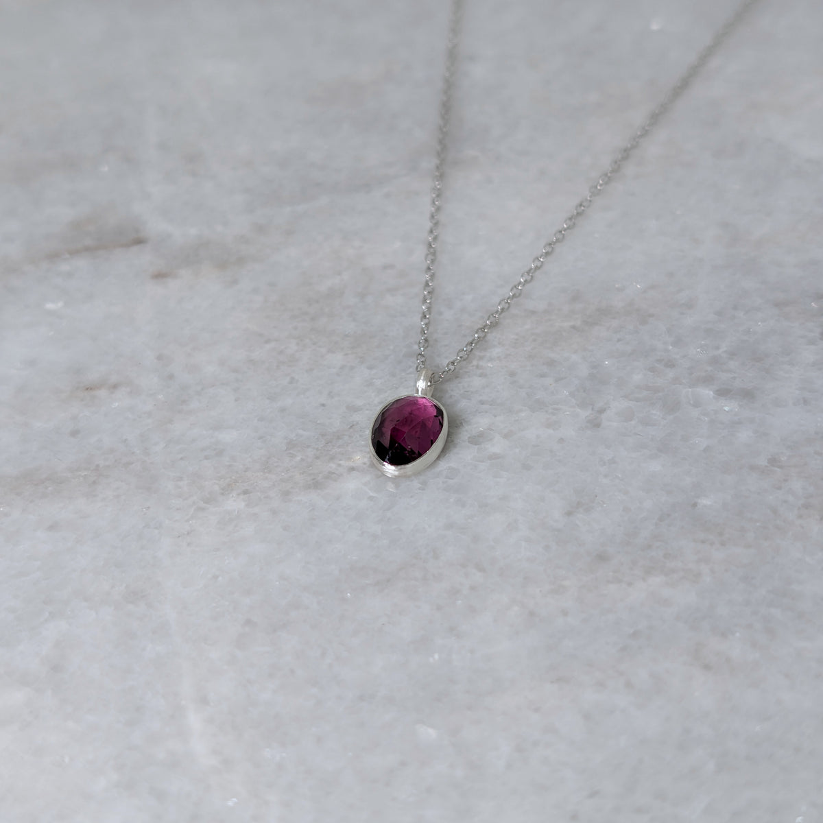 Silver necklace with a warm purple stone pendant on a white marble surface