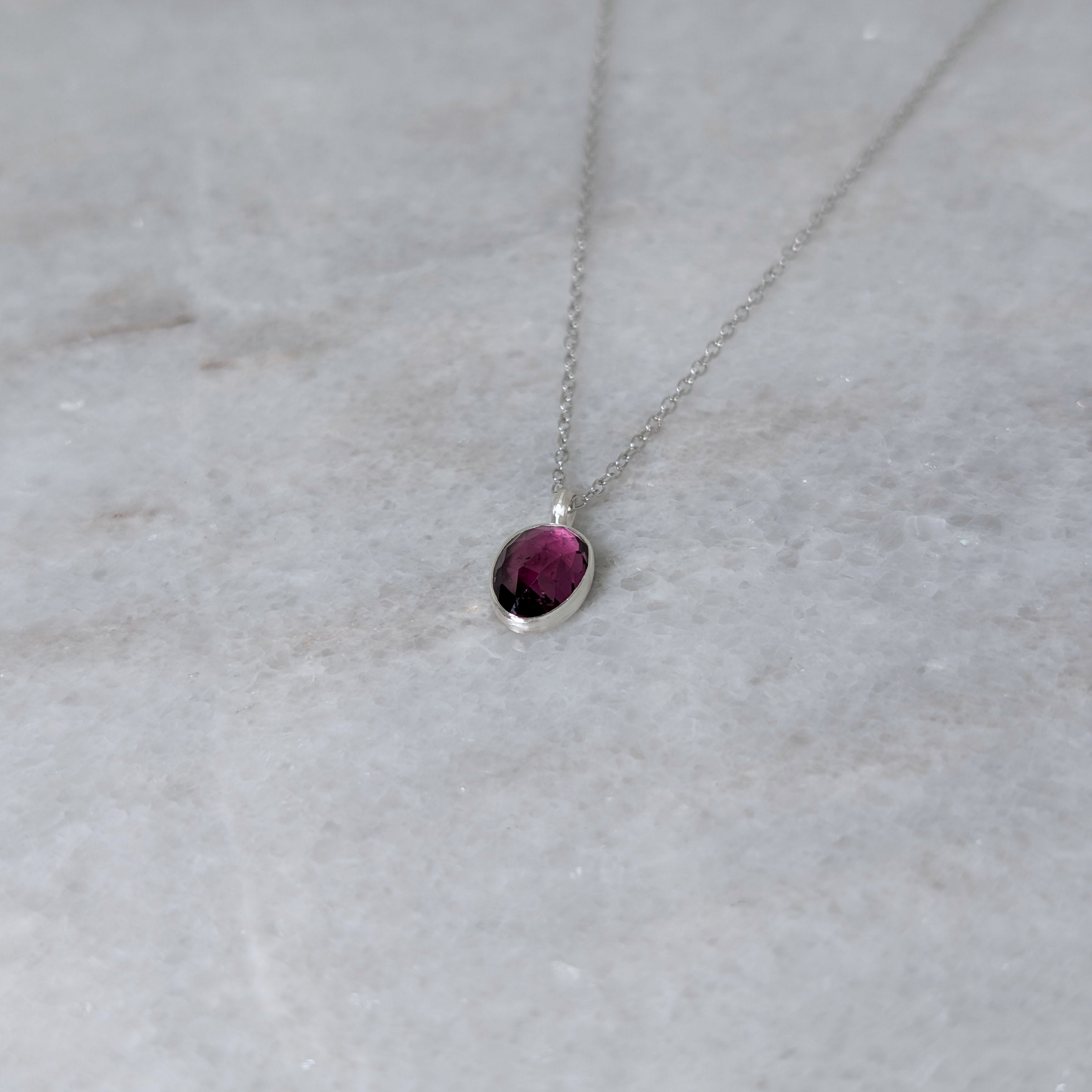 Silver necklace with a warm purple stone pendant on a white marble surface