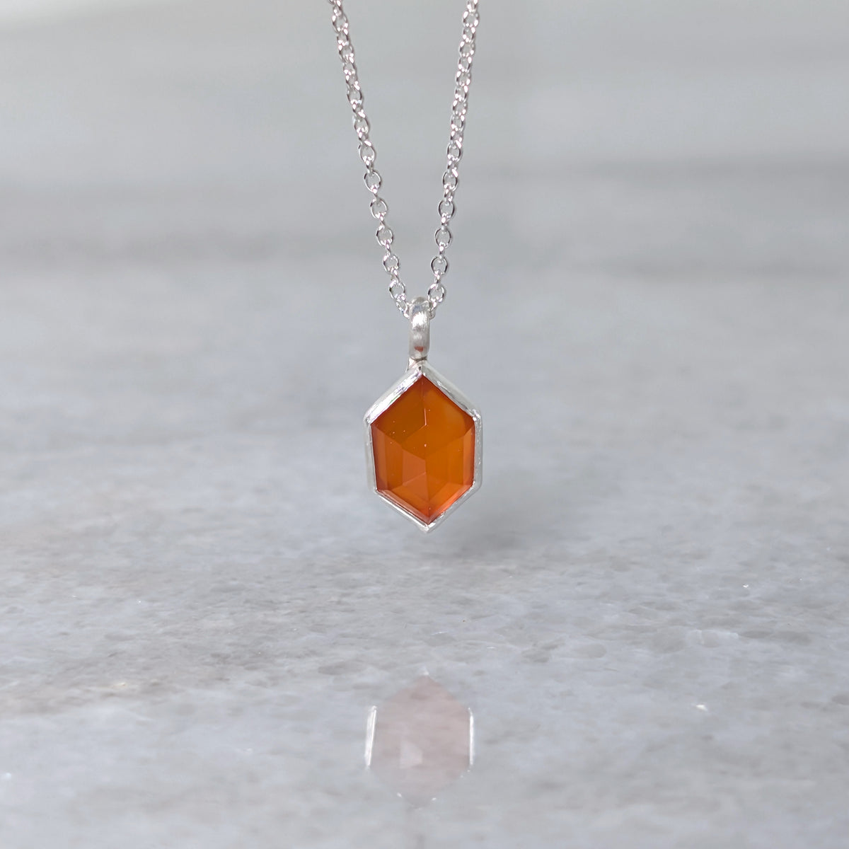 Necklace with a hexagonal orange stone set in a silver bezel on a gray background