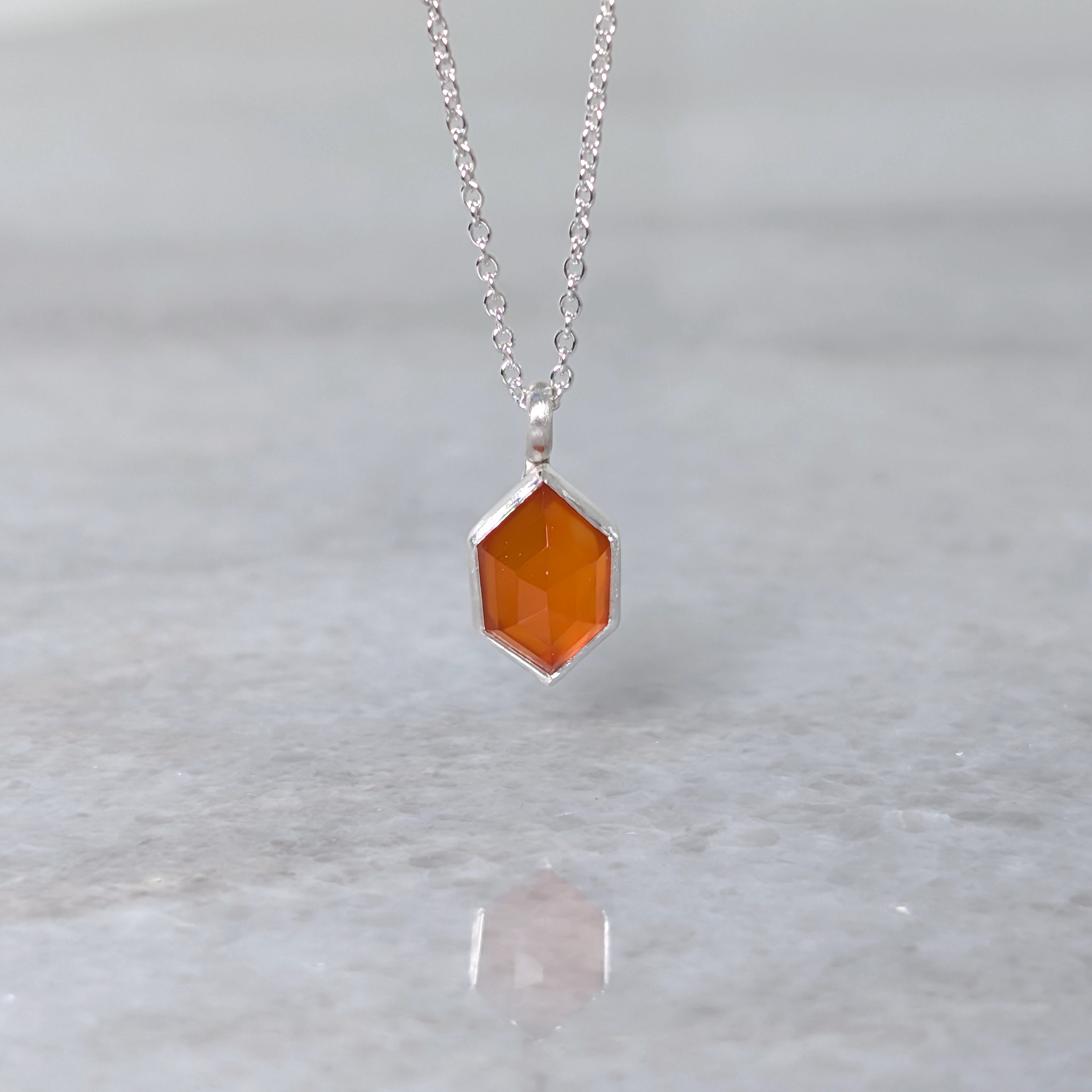Necklace with a hexagonal orange stone set in a silver bezel on a gray background