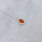 angled view of a necklace with a hexagonal orange stone set in a silver bezel on a gray background