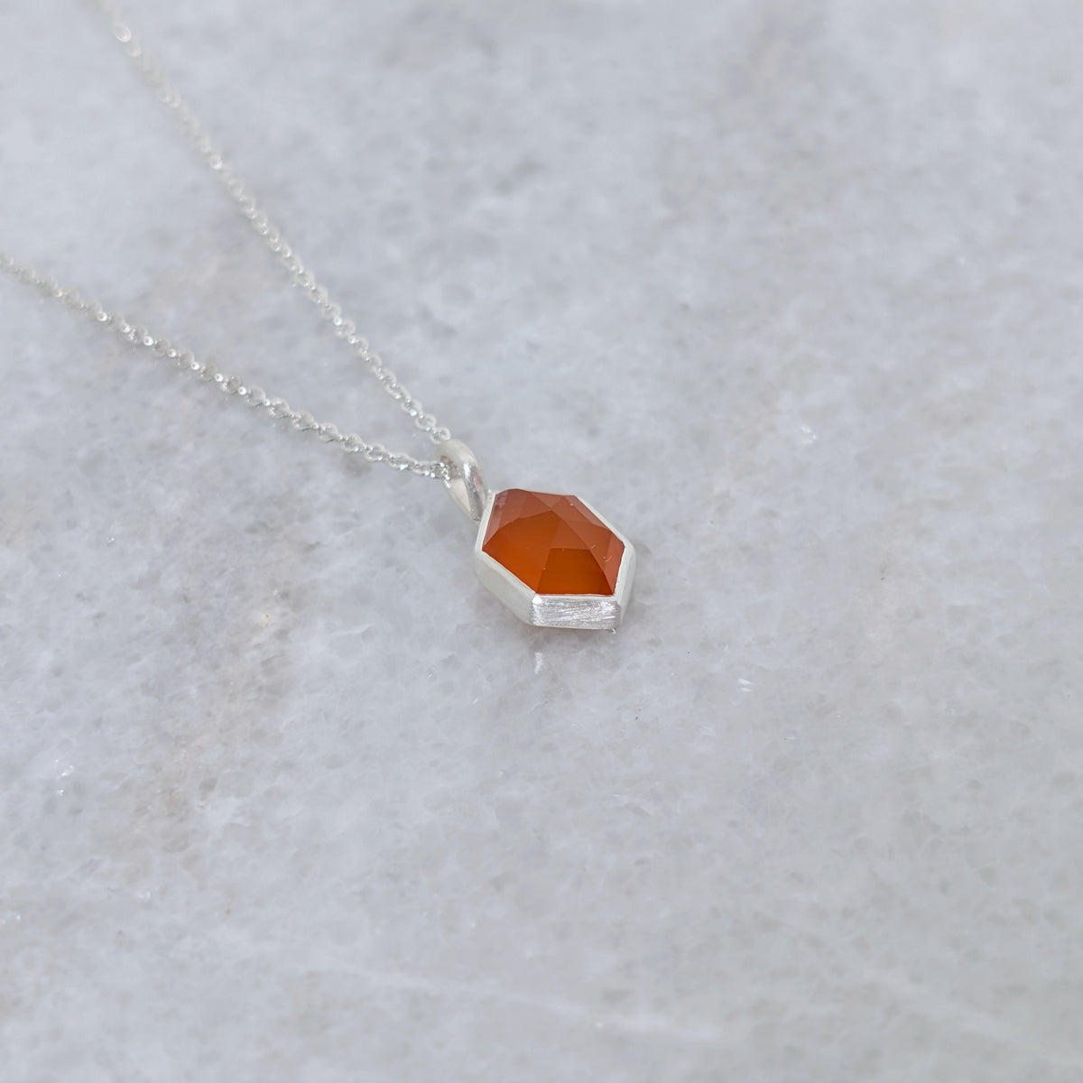 angled view of a necklace with a hexagonal orange stone set in a silver bezel on a gray background