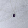 Silver necklace with a purple stone pendant on a marble surface