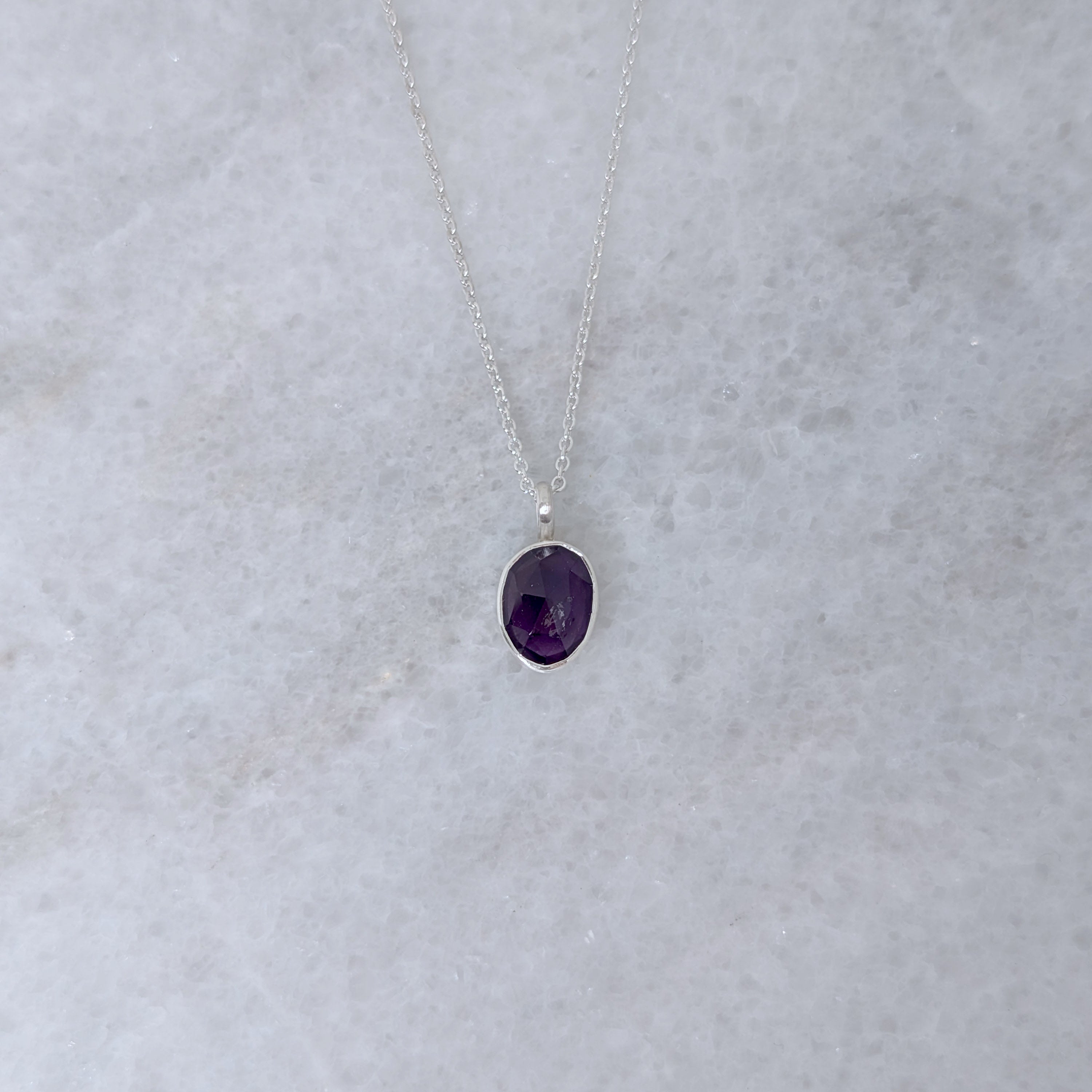 Silver necklace with a purple stone pendant on a marble surface