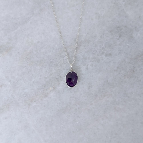 Silver necklace with a purple stone pendant on a marble surface