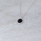 Angled view of Silver necklace with a purple stone pendant on a marble surface
