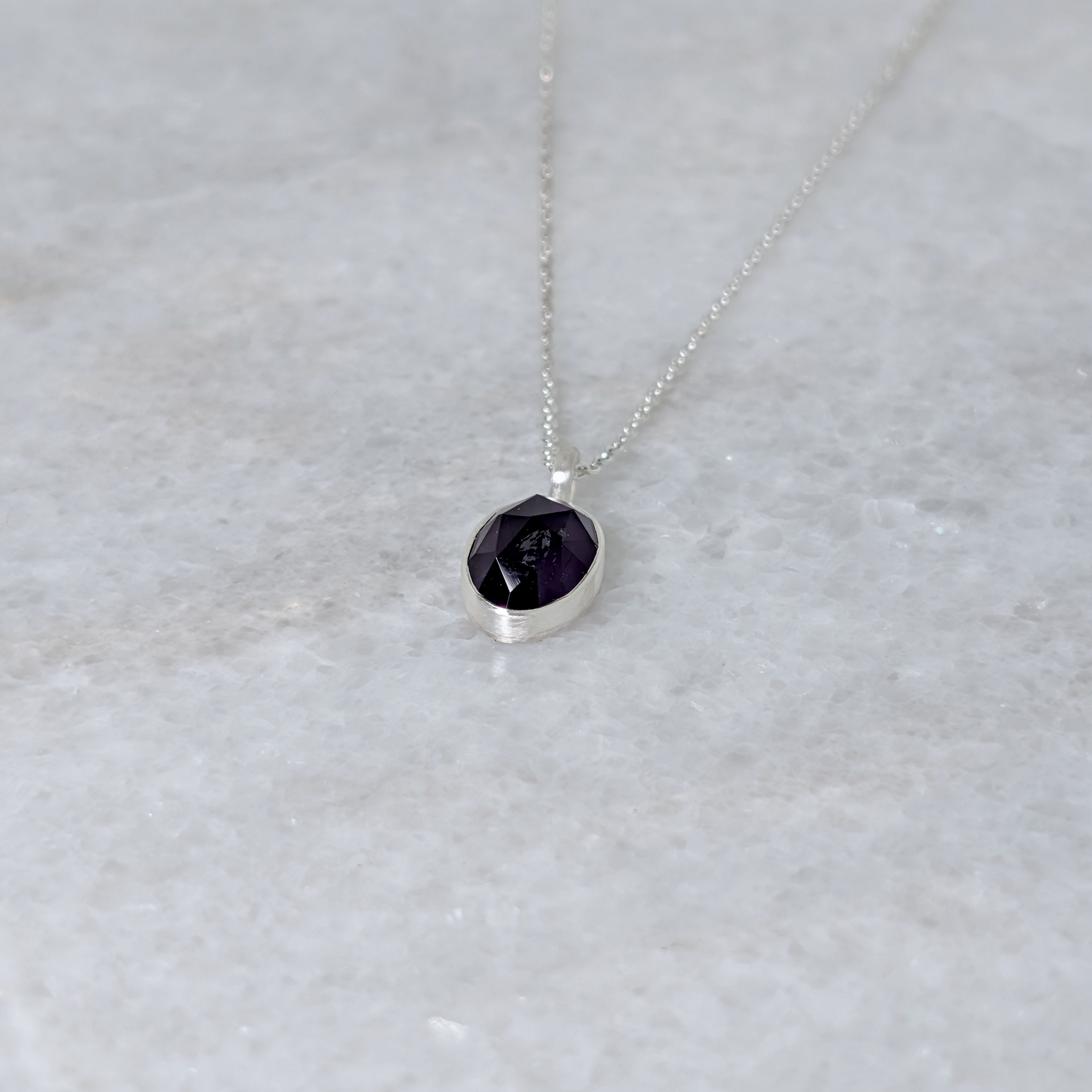 Angled view of Silver necklace with a purple stone pendant on a marble surface