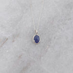 Silver necklace with a blueish purple pendant with vine motifs on a white marble surface