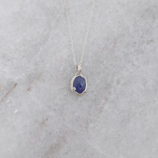 Silver necklace with a blueish purple pendant with vine motifs on a white marble surface