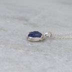 Side view of a silver pendant with a bluish purple stone and vine motifs on a white marble surface