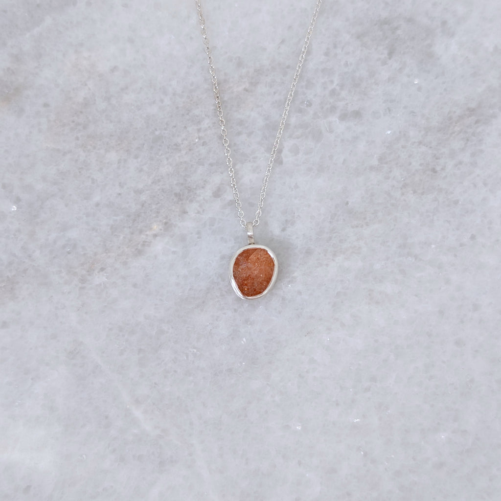 Necklace with a speckled orange stone set in a silver bezel on a white marble backround