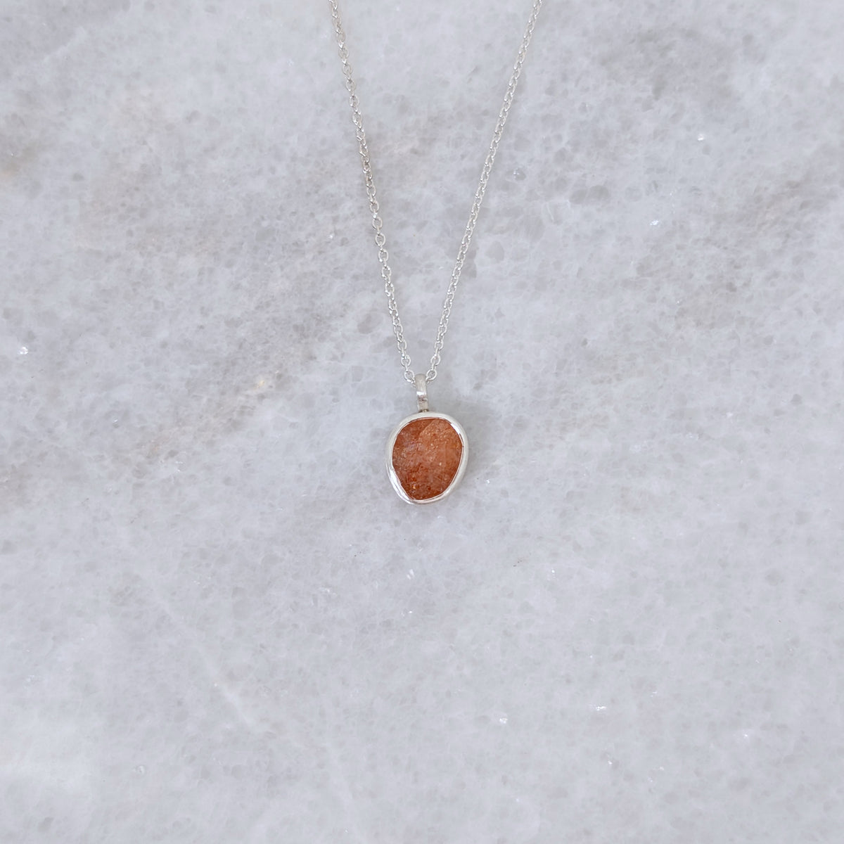 Necklace with a speckled orange stone set in a silver bezel on a white marble backround