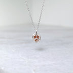 The back side of a silver pendant with an orange speckled stone visible through windows framed by silver vine motifs