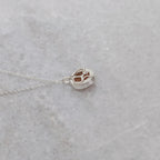 The back side of a silver necklace with an orange speckled stone visible through windows framed by silver vine motifs