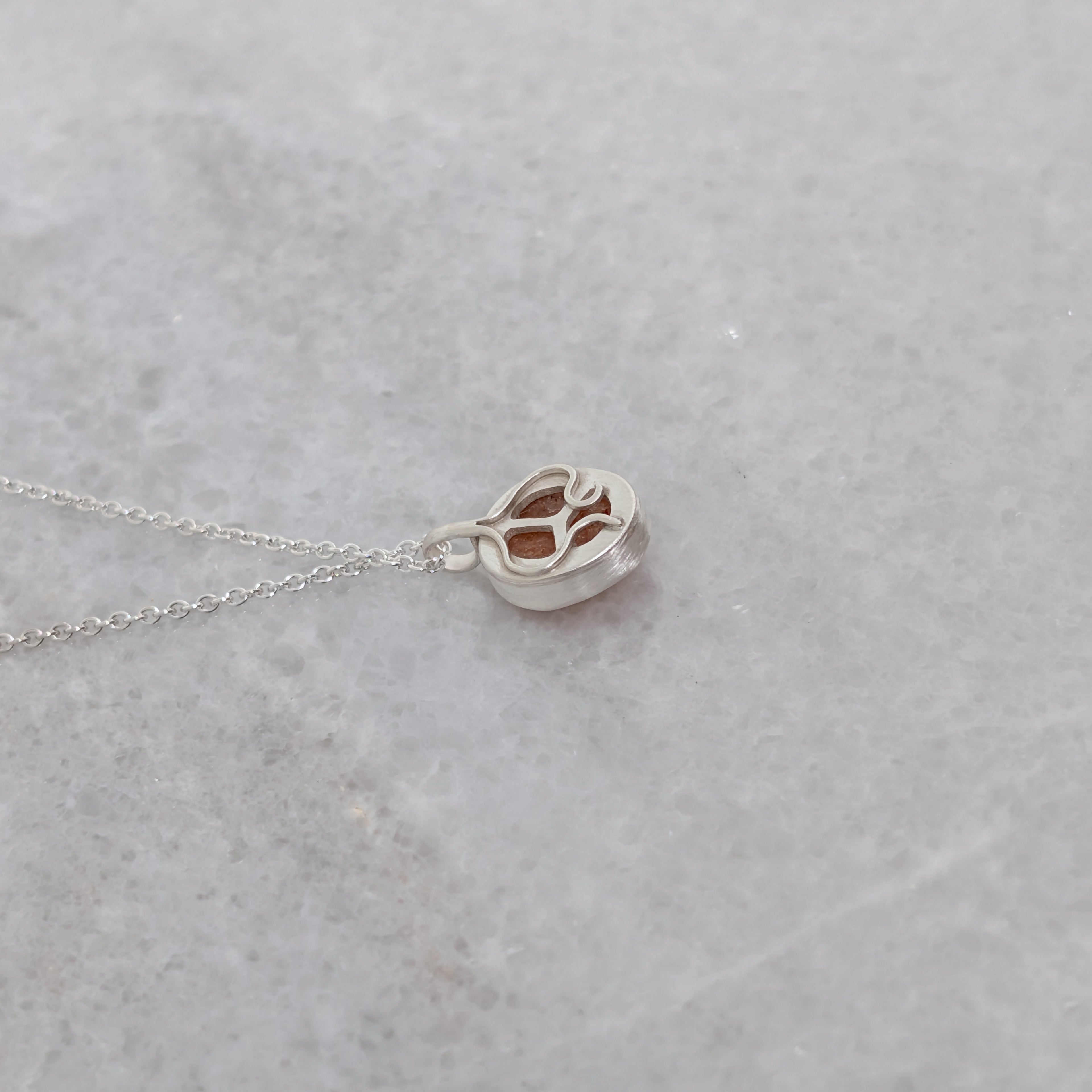 The back side of a silver necklace with an orange speckled stone visible through windows framed by silver vine motifs