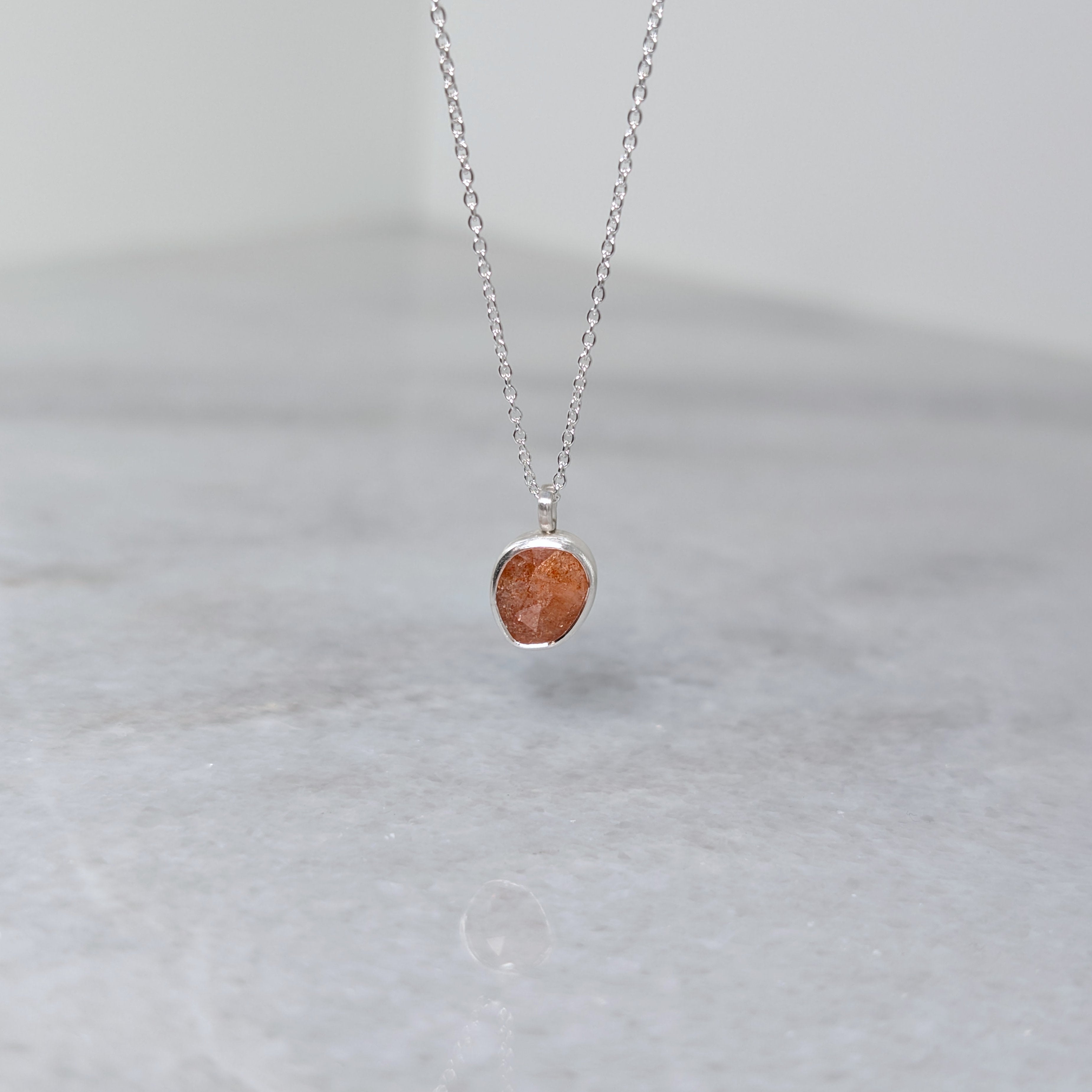 Silver necklace with an orange stone pendant on a white marble background