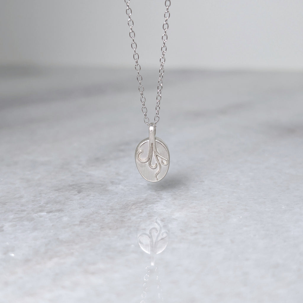 Back view of a silver necklace with four curling vine details on the back of the bezel, on a white marble background