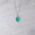 Silver necklace with a teal colored stone in a silver bezel on a white marble background