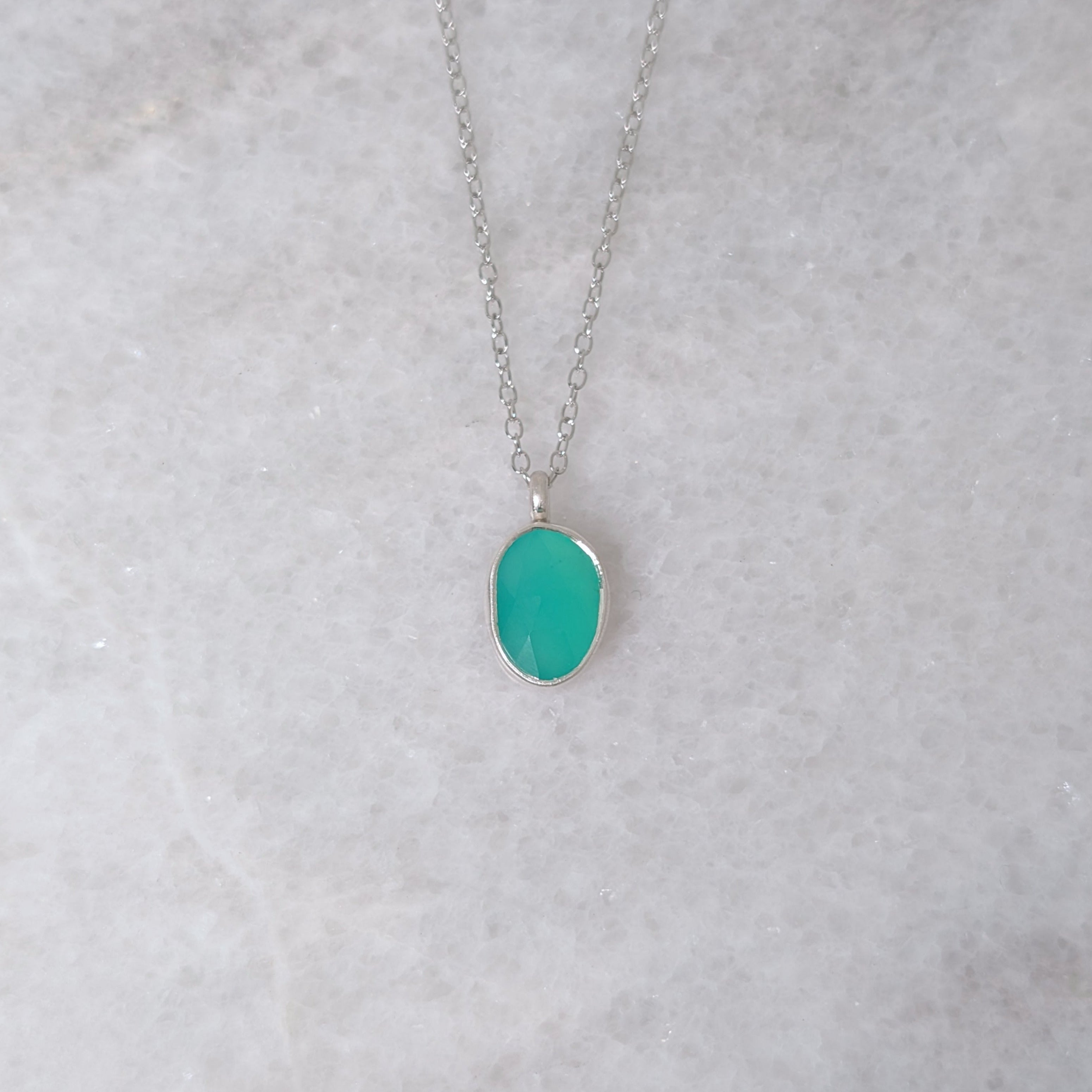 Silver necklace with a teal colored stone in a silver bezel on a white marble background