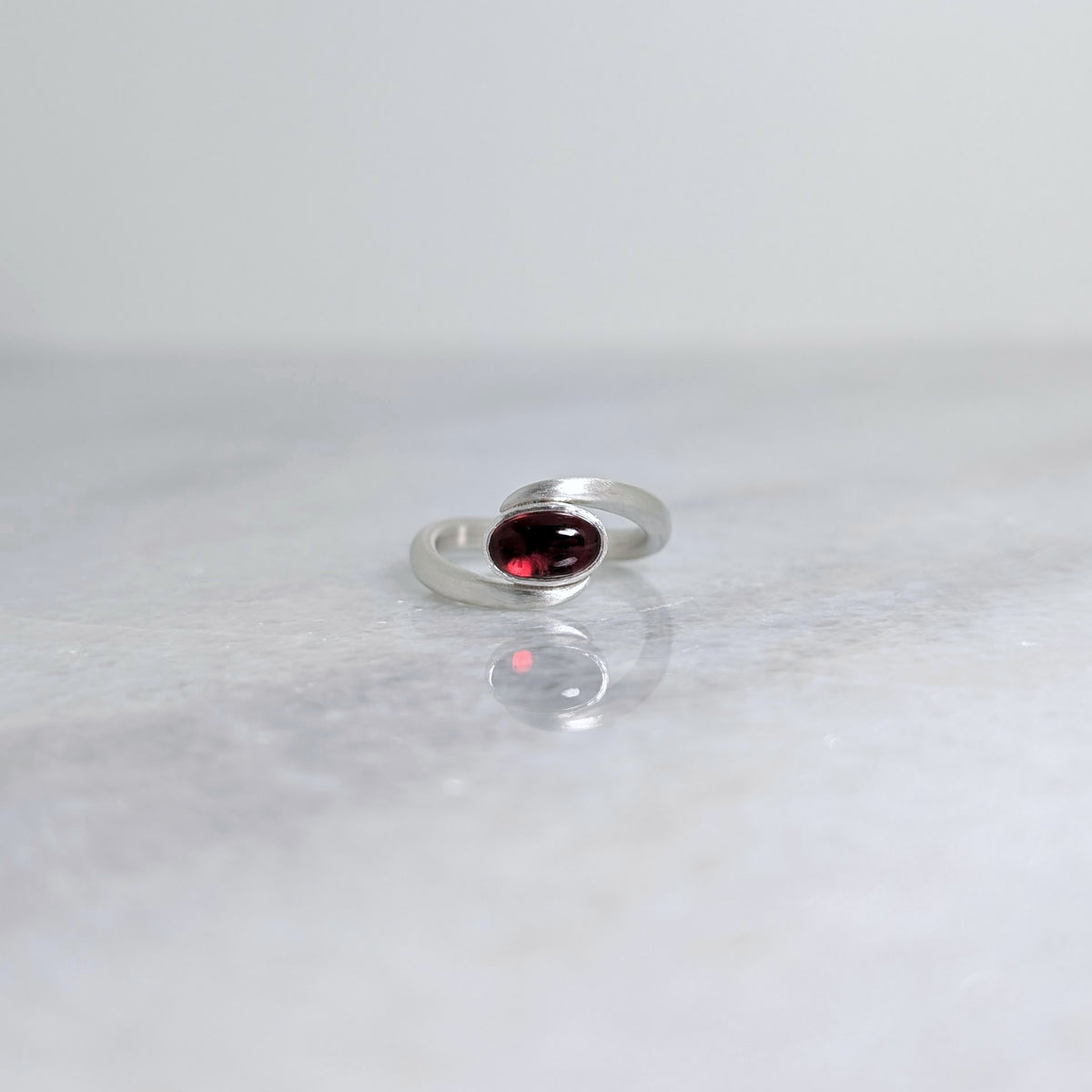 Matte Silver ring wrapped around bezel set red garnet oval cabochon