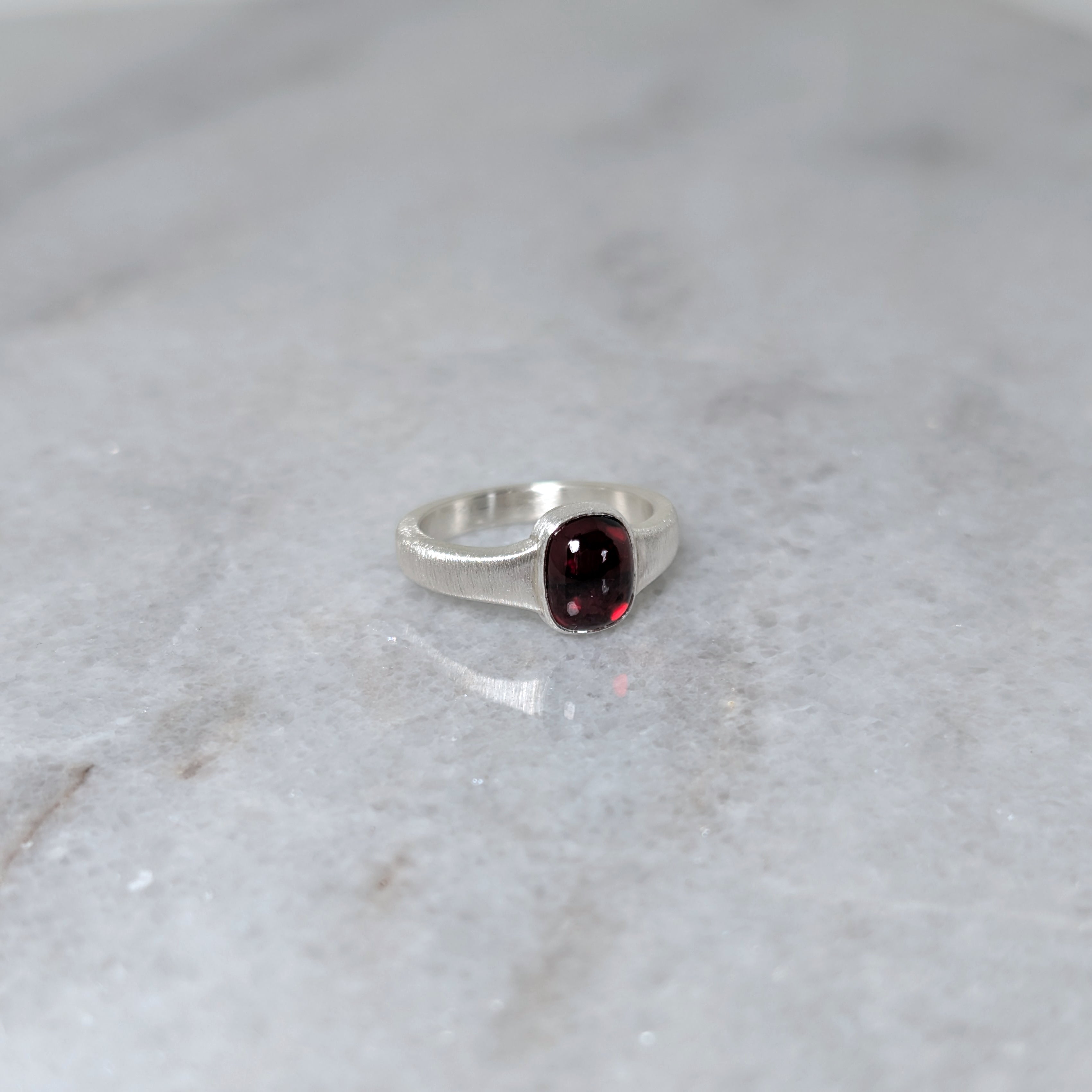 Angled view of silver ring with a garnet center stone on a white marble surface